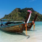 Two traditional longtail boats docked on a pristine tropical beach against a backdrop of lush islands.
